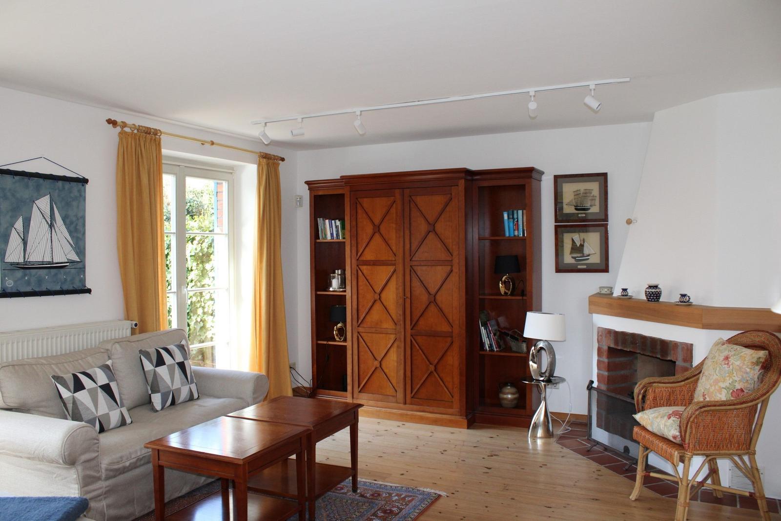 Wohnzimmer mit Sofa, Holzmöbel und Kamin. Fenster mit gelben Vorhängen.
