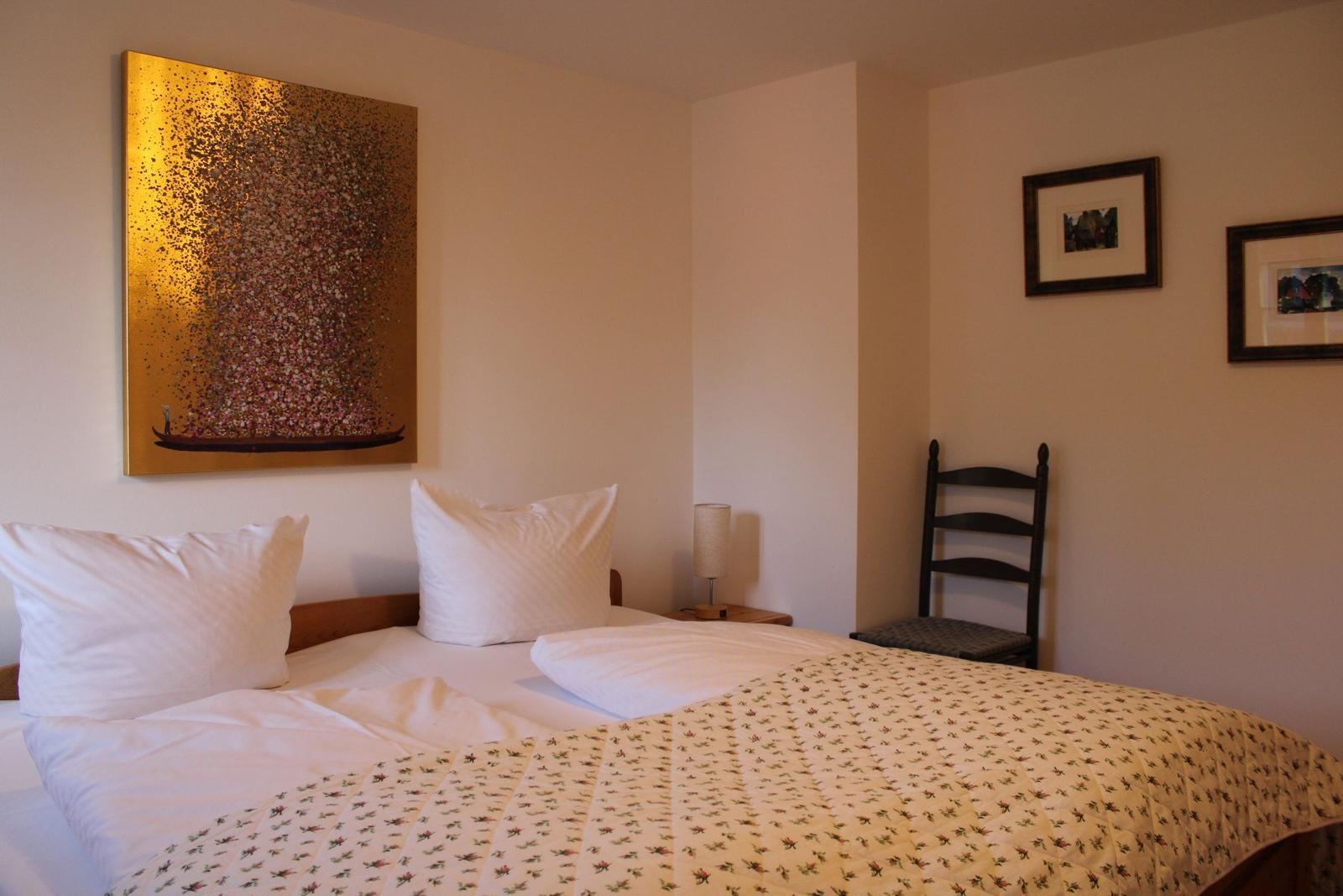 Schlafzimmer mit Bett, Stuhl und Wandbildern.