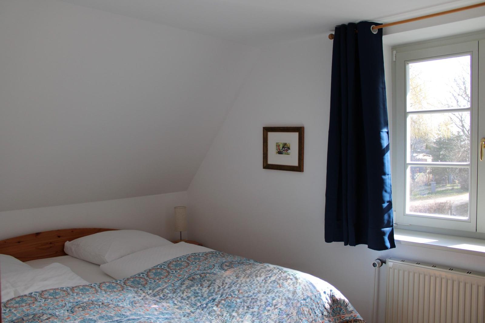 Schlafzimmer mit Dachschrägen, Bett, Fenster und Vorhang.