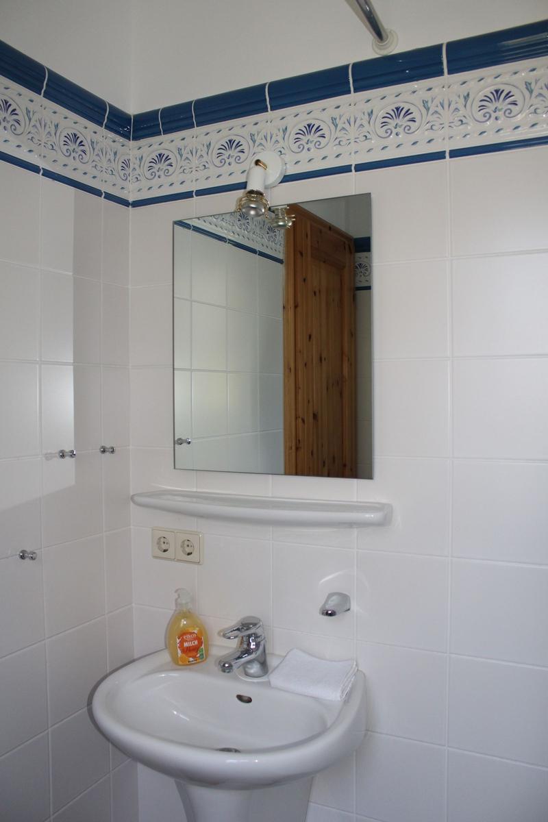 Badezimmer mit Waschbecken, Spiegel und blau-weißem Fliesendekor an den Wänden.