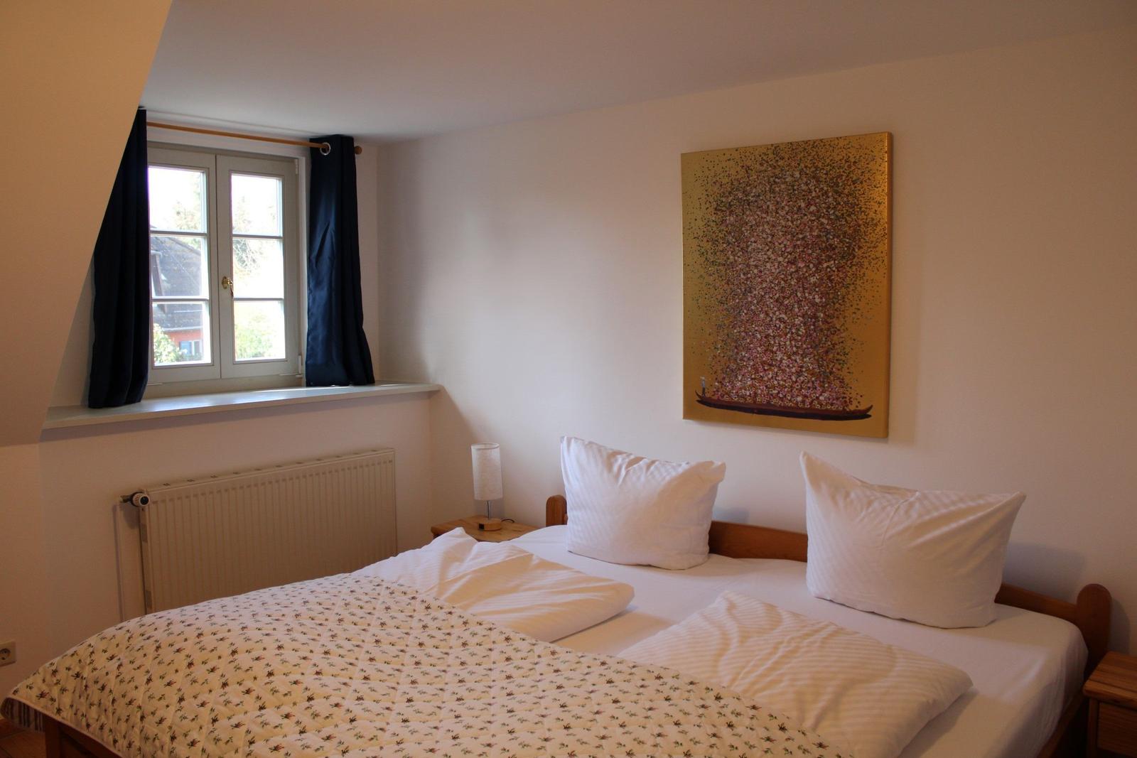 Schlafzimmer mit Bett, Fenster und Wandbild.