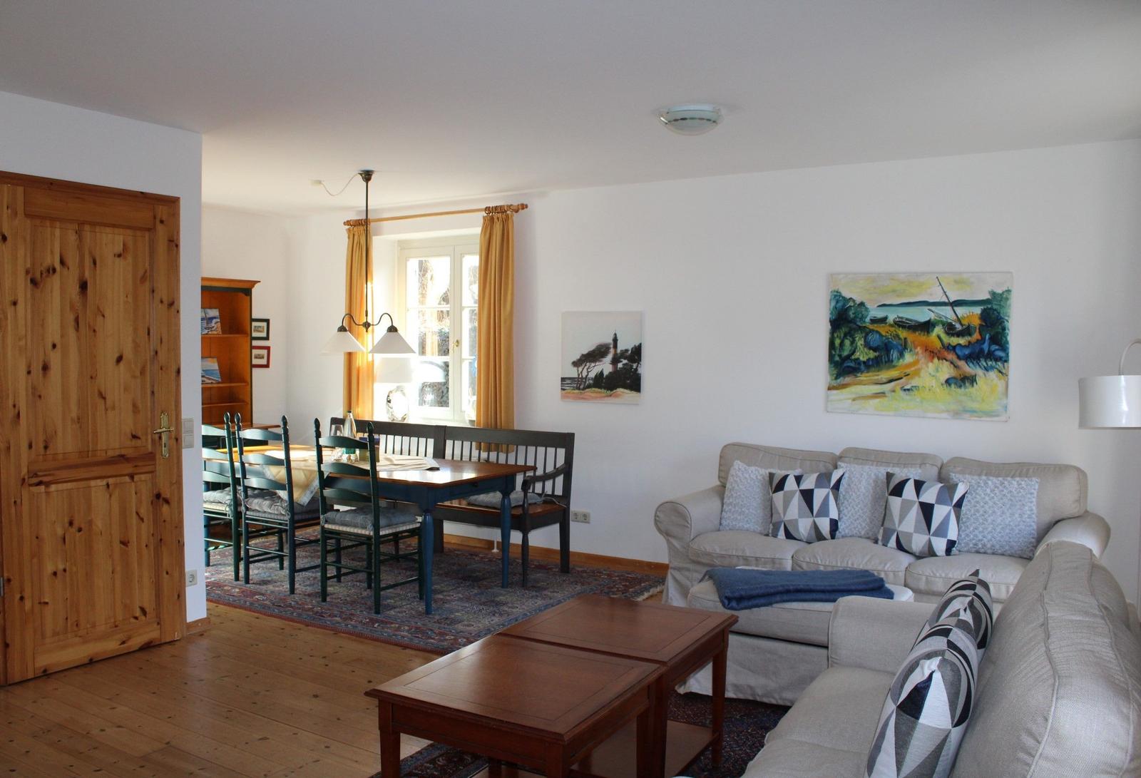 Wohn- und Essbereich mit Sofa, Tisch und Stühlen. Holztür und Wandbilder sichtbar.
