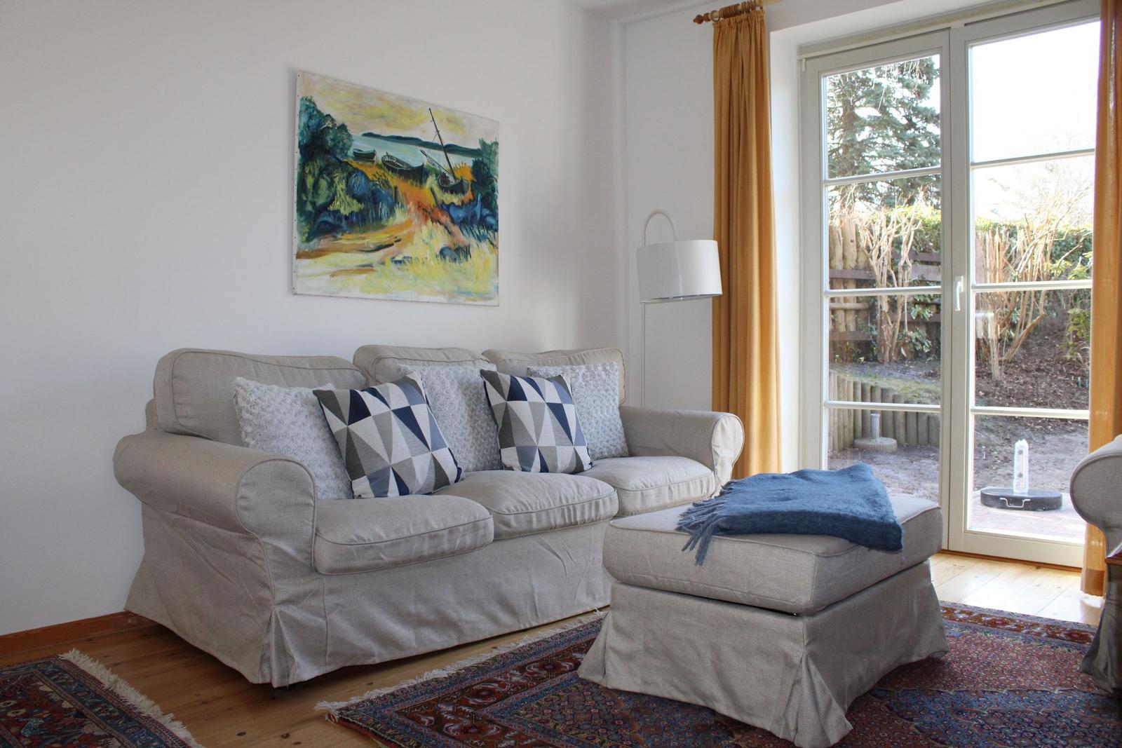 Ein Wohnzimmer mit einem Sofa, Kissen, einem Sitzhocker und einem Wandbild.