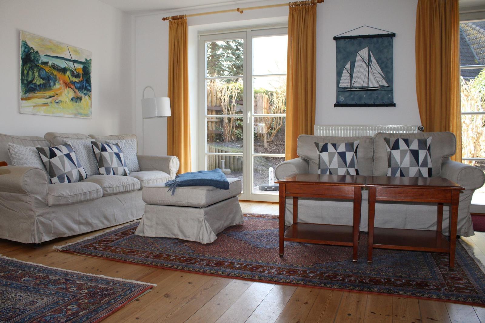Wohnzimmer mit zwei Sofas, Tisch, Teppich und Fenster zur Außenterrasse.
