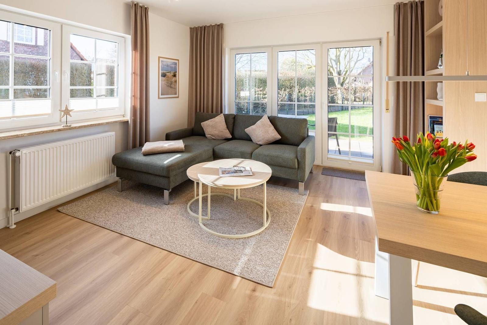 Wohnzimmer mit grauem Sofa, runden Tisch und Blick auf Garten.