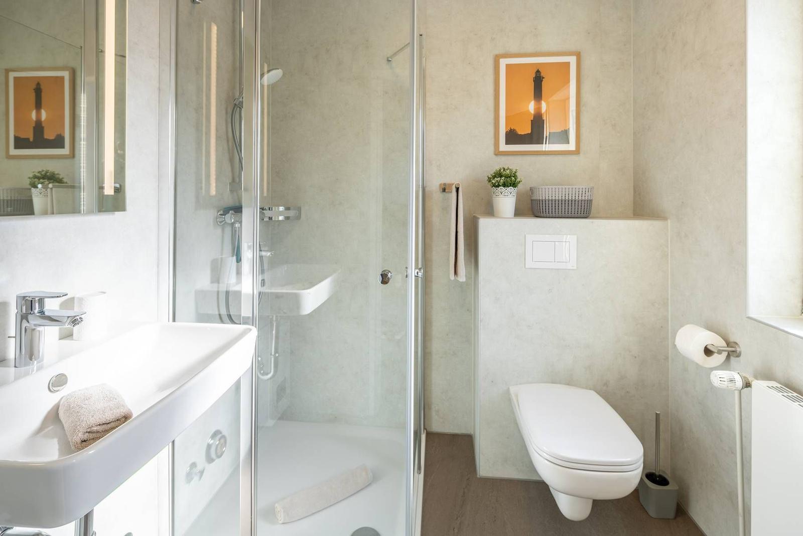 Badezimmer mit Dusche, Waschbecken und Toilette. Wandbild zeigt Leuchtturm.