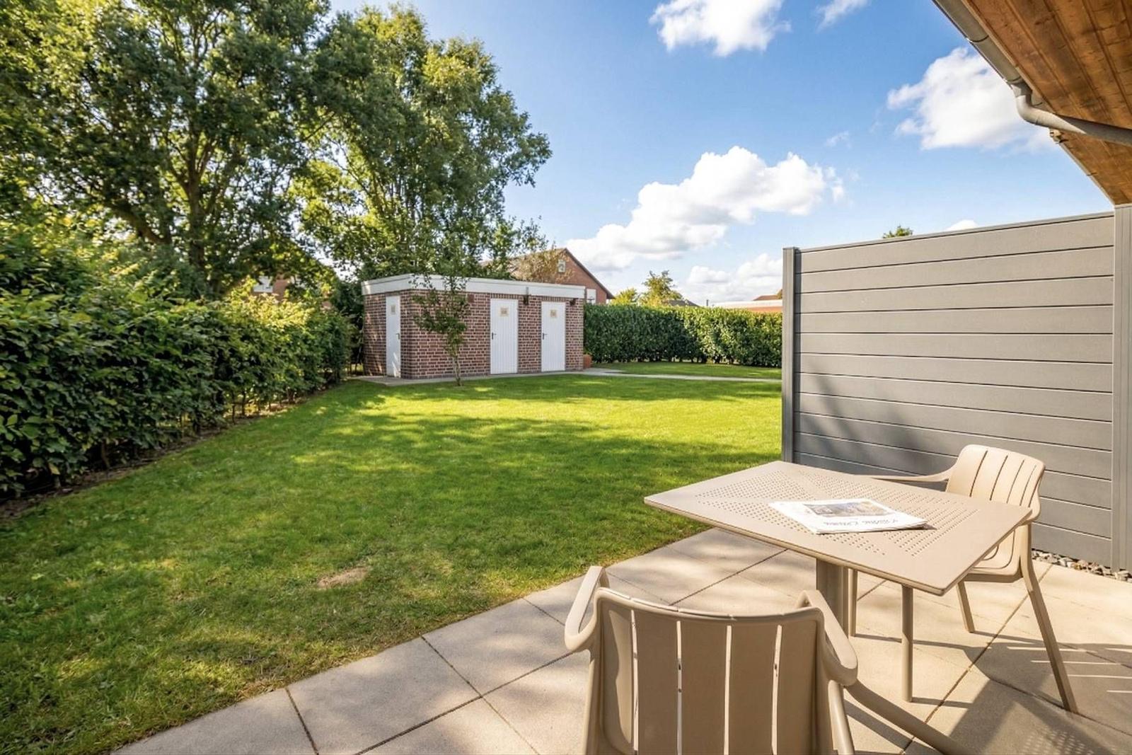 Terrasse mit Tisch und Stühlen, Blick auf grünen Garten und Holzschuppen.