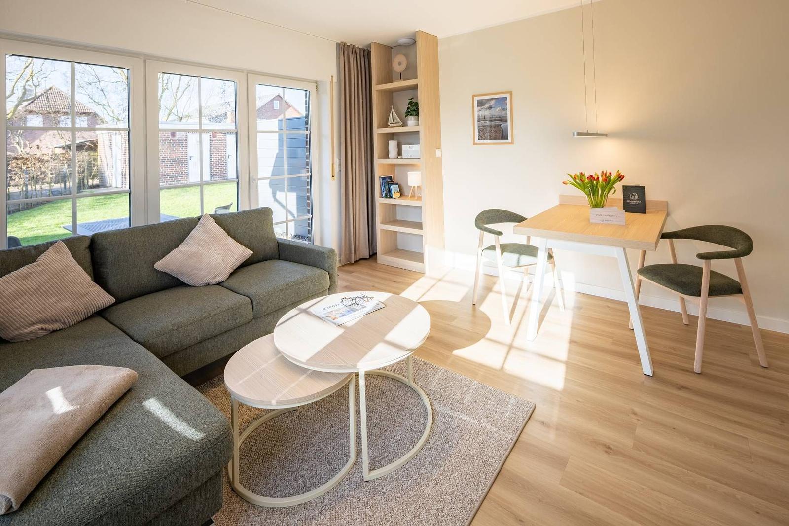 Wohn- und Essbereich mit Sofa, Tisch und Stühlen. Große Fenster und Holzboden.