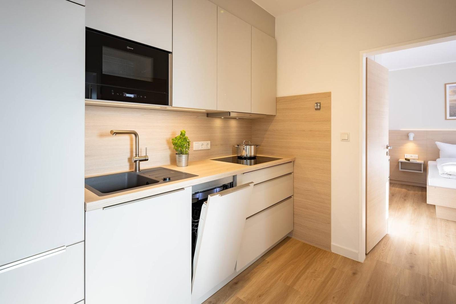 Küche mit Spüle, Dunstabzug und integriertem Mikrowellenherd. Durchgang zur Schlafzimmer.