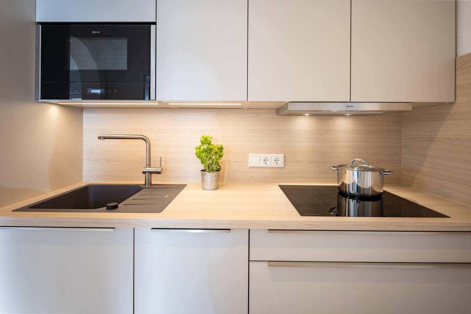 Moderne Küche mit Edelstahlspüle, Kochfeld und eingebauter Mikrowelle.