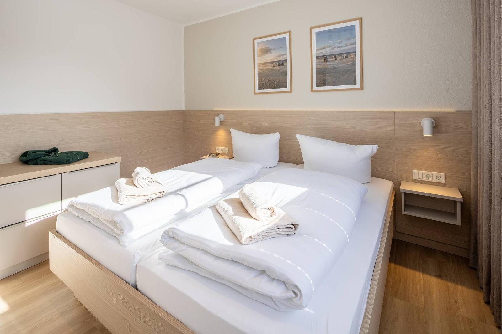 Doppelbett mit weißen Bettwäsche und Handtüchern. Holzwand und Bilder an der Wand.