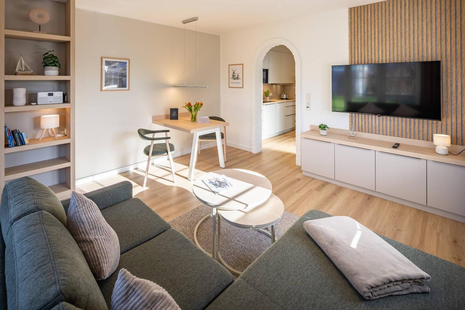 Wohnzimmer mit Sofa, Couchtisch und Fernseher. Essbereich und Küche im Hintergrund.