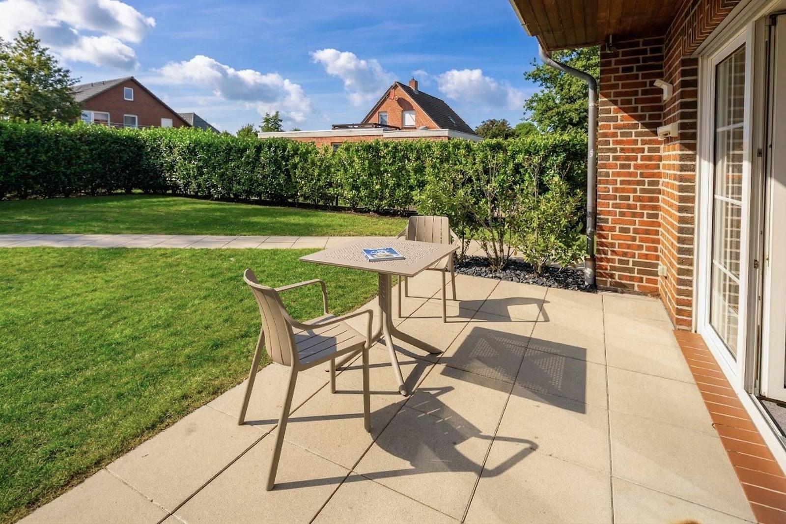 Terrasse mit Tisch und Stühlen, Blick auf grünen Rasen und Hecke.