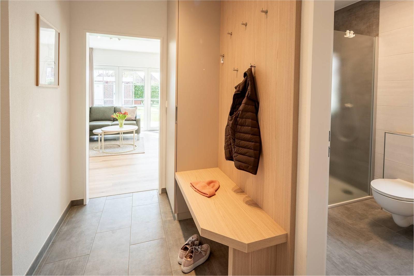 Flur mit Garderobe, Sitzbank und Blick in Wohn- und Badezimmer.