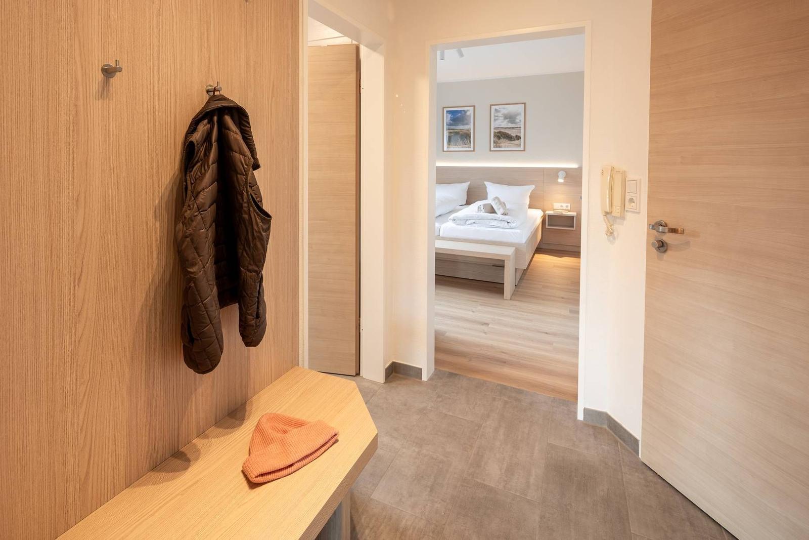 Hallen mit Holzwand, Jacke und Mütze. Blick in Schlafzimmer mit Bett und Bildern.