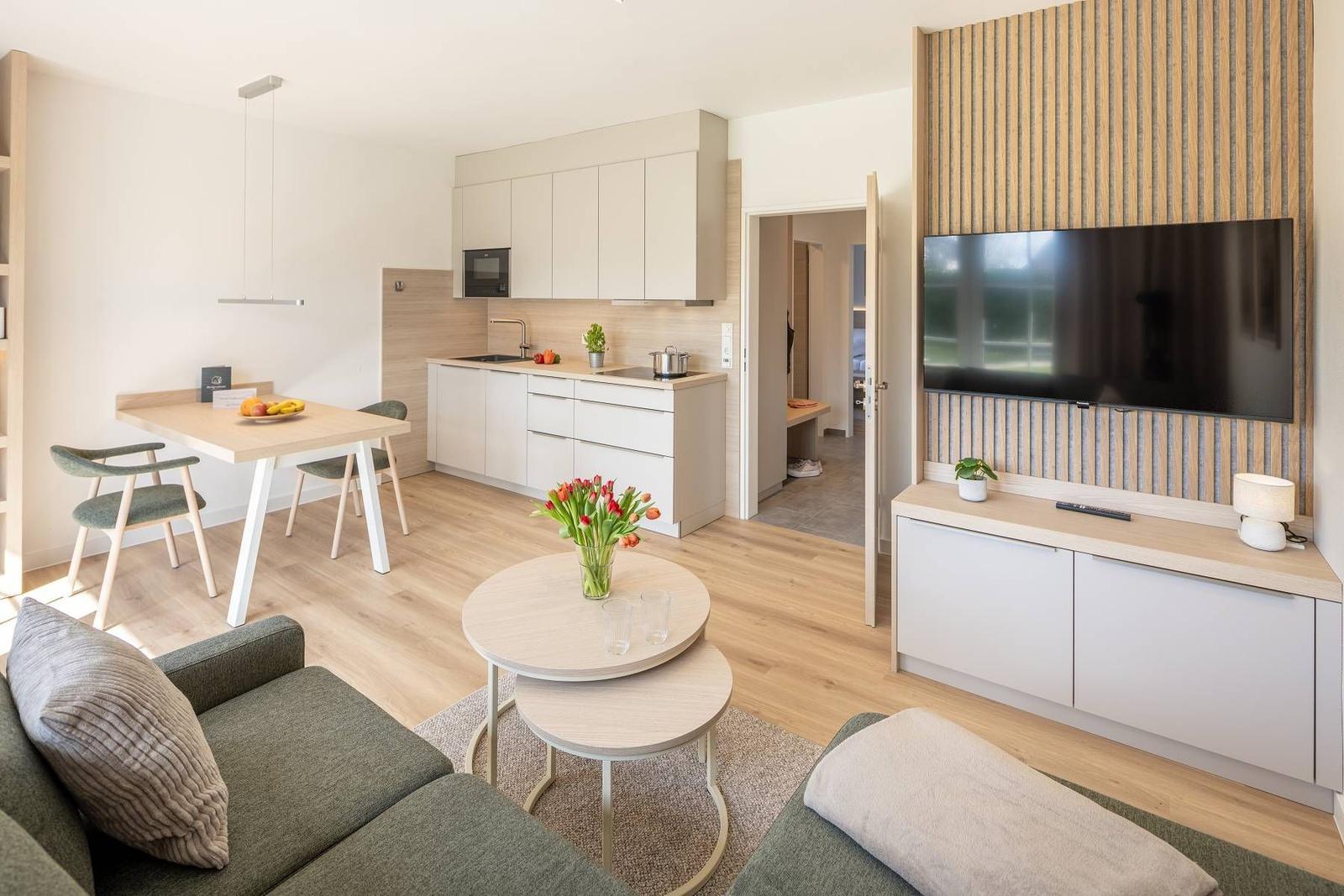 Wohnbereich mit Küche, Esstisch und TV. Holzboden und moderne Einrichtung.