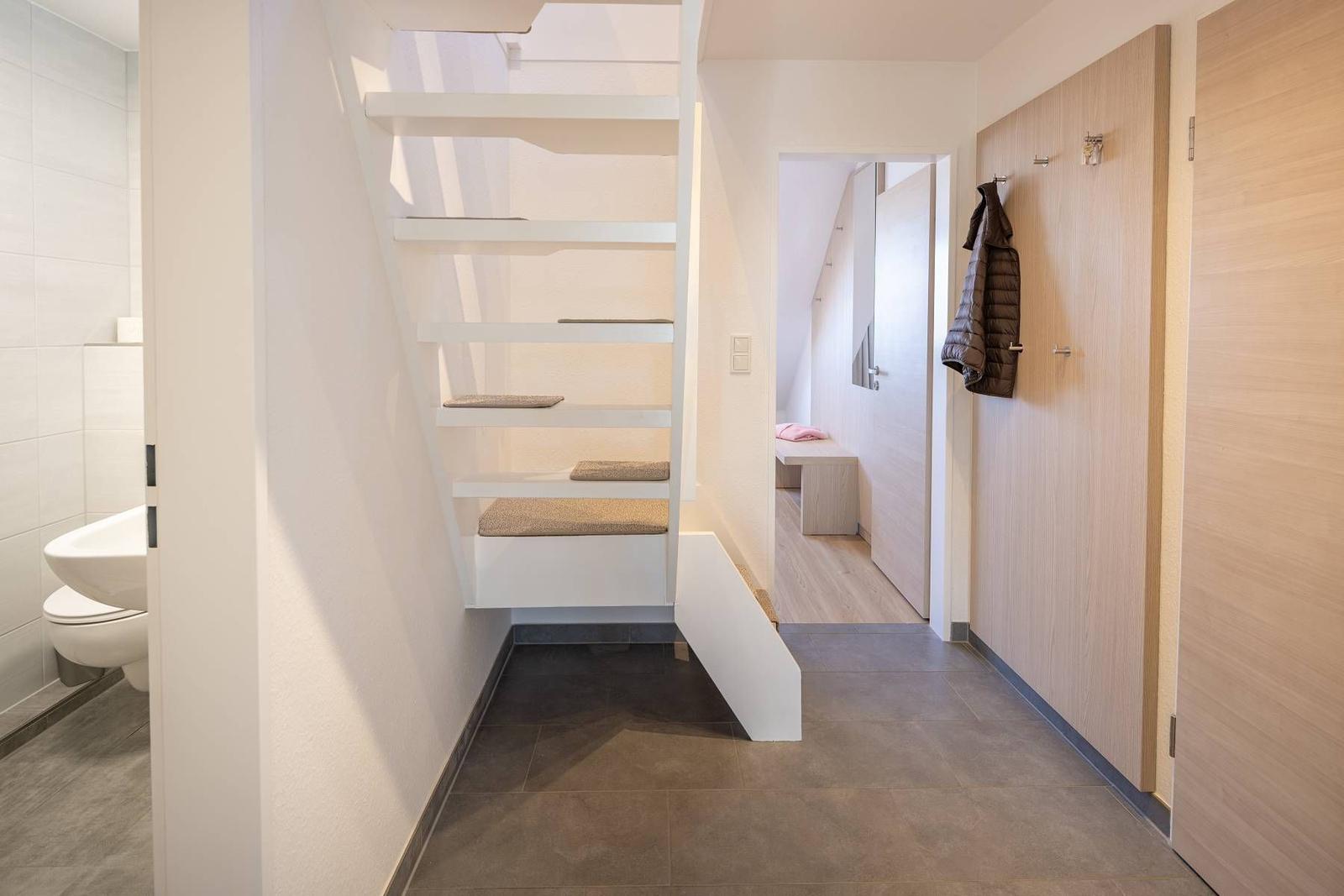 Hinter dem Treppenhaus ist ein Flur mit Kleiderhaken und eine Tür zum Schlafzimmer.