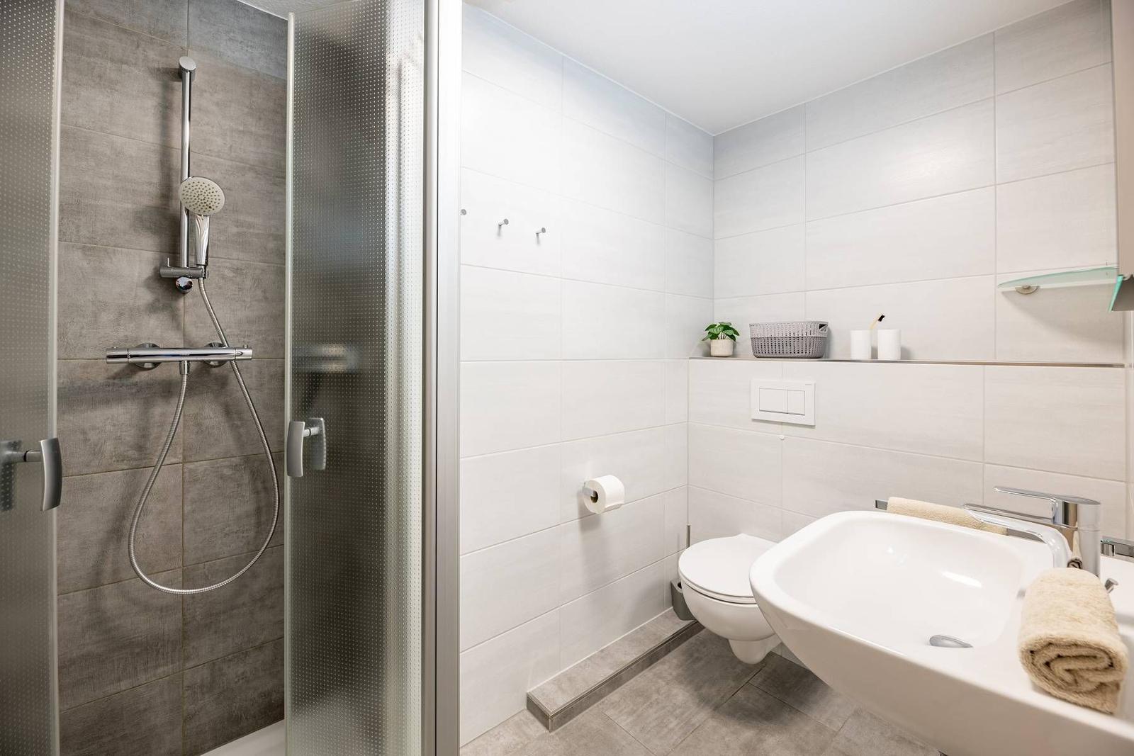 Badezimmer mit Dusche, Toilette und Waschbecken. Fliesen und moderne Einrichtung.