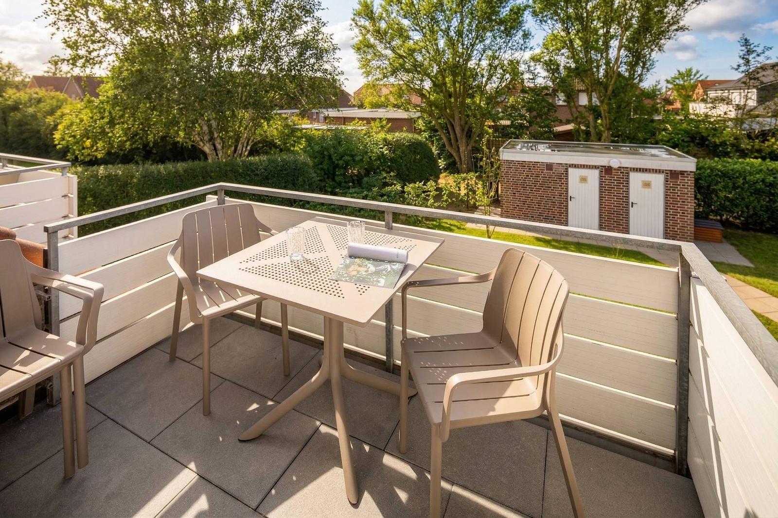Terrasse mit Tisch und Stühlen, Blick auf Garten und Gebäude.