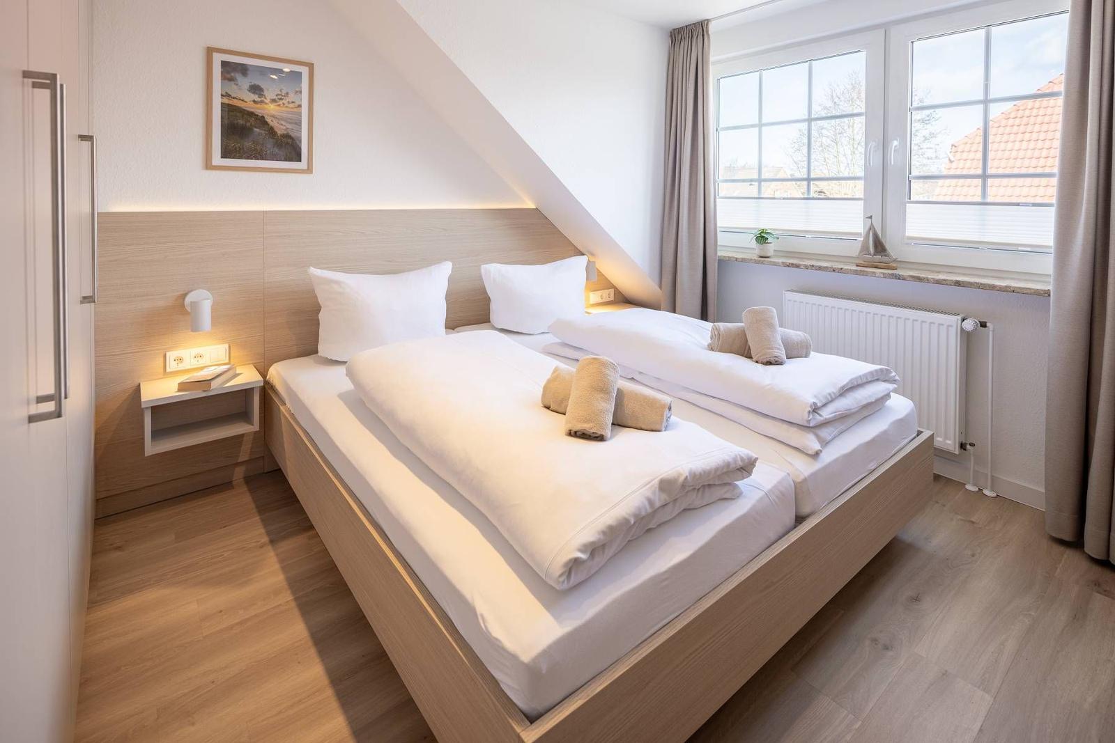 Schlafzimmer mit Doppelbett, Fenster und Holzboden.