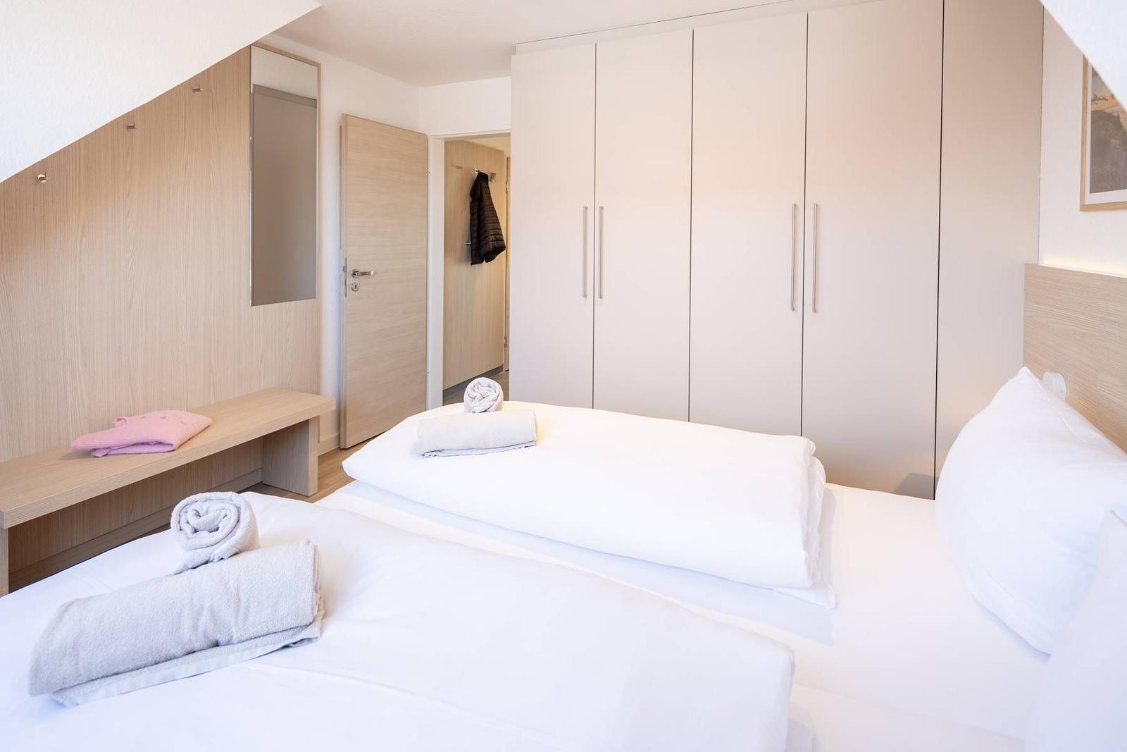 Schlafzimmer mit Doppelbett, weißen Laken und Holzmöbeln. Großer Schrank und Spiegel an der Wand.