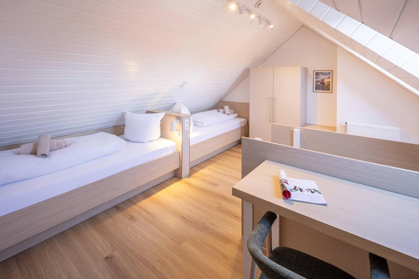 Zimmer mit zwei Betten, Schreibtisch und Dachschräge mit Dachfenster.