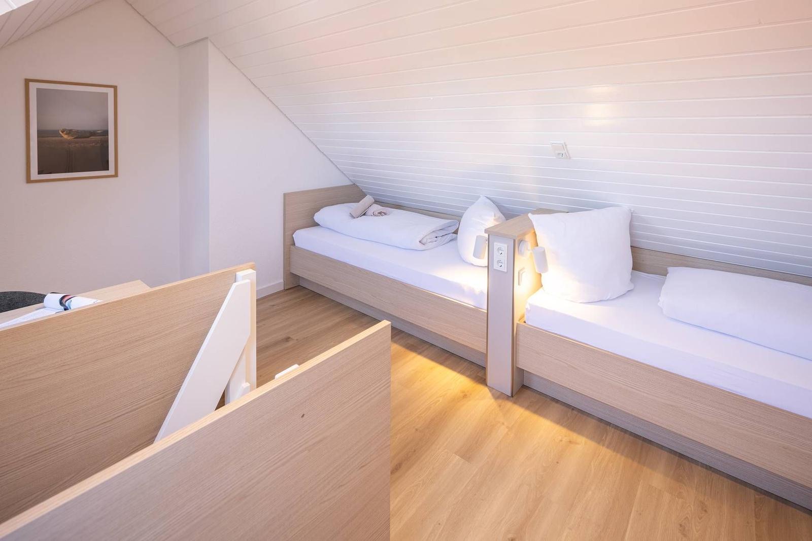 Zwei Einzelbetten mit weißen Laken und Kissen an einer schrägen Wand mit Holzvertäfelung.