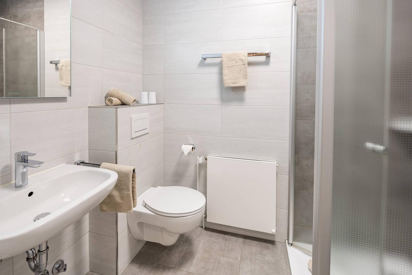 Badezimmer mit Dusche, Toilette und Waschbecken mit Spiegel.