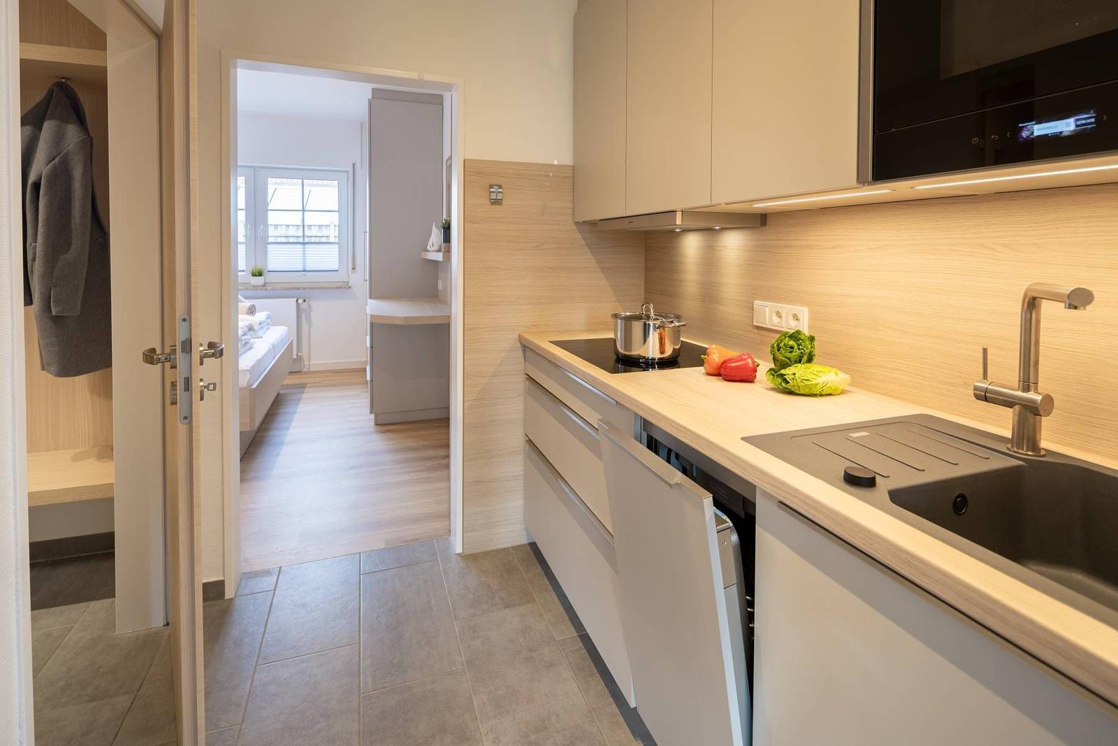 Küche mit Arbeitsplatte, Spüle und Kochfeld. Im Hintergrund ist ein Schlafzimmer sichtbar.