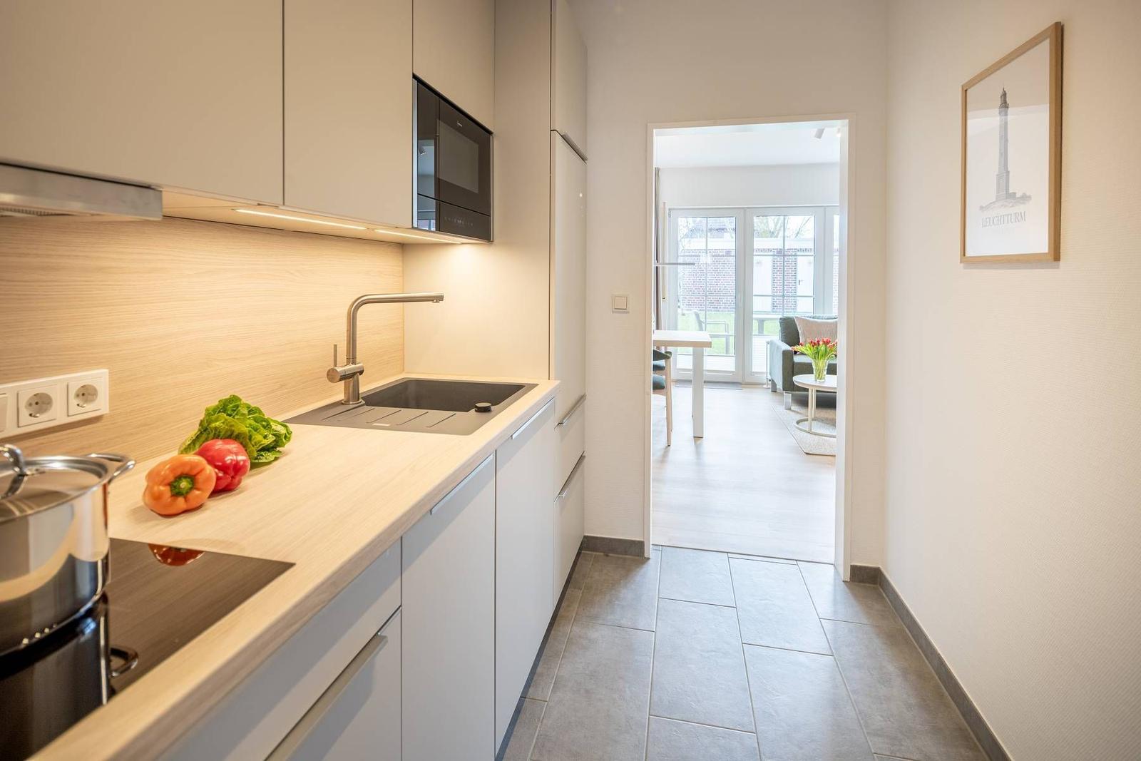 Küche mit Arbeitsplatte, Spüle und Mikrowelle. Durchgang zum Wohnbereich mit Tisch und Sofa.
