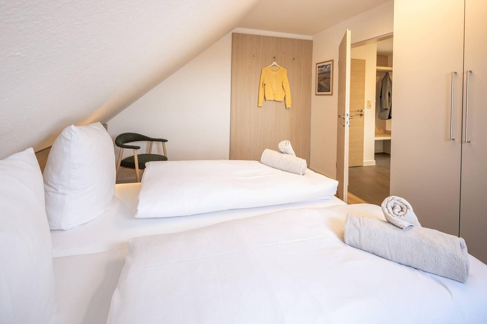 Schlafzimmer mit Doppelbett, Schrank und Kleiderständer. Tür führt in Badezimmer.