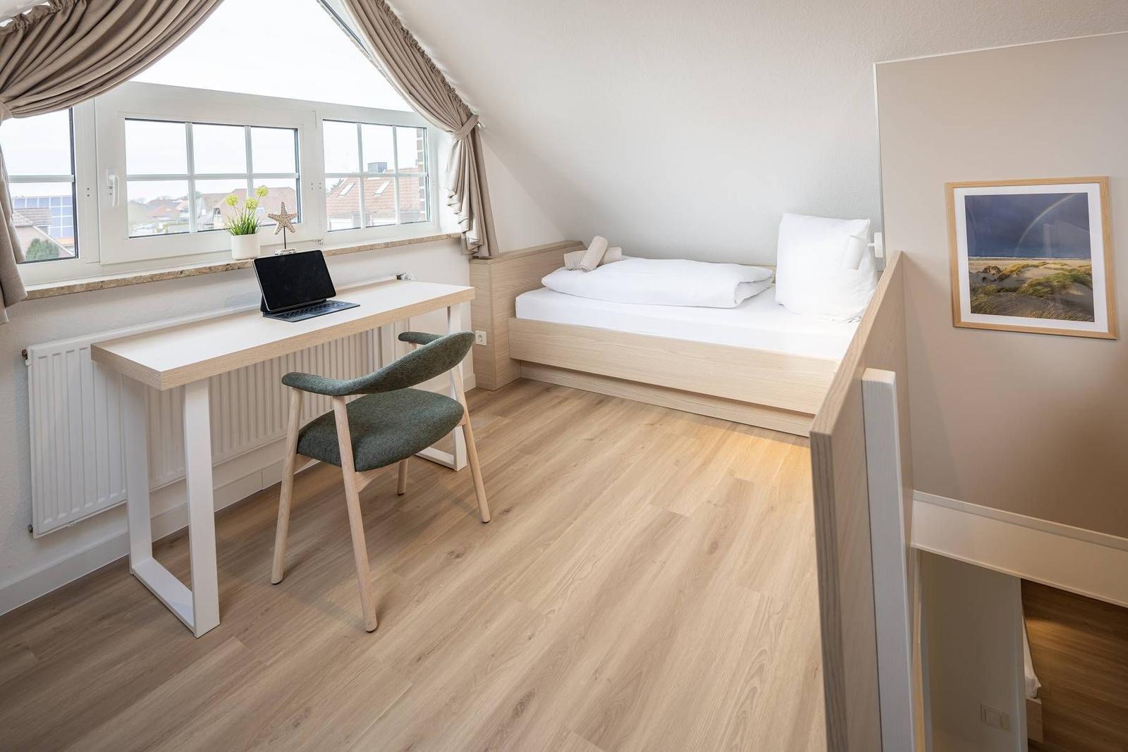 Ein Schlafzimmer mit Bett, Schreibtisch und Fenster. Holzfußboden und Wandbild.