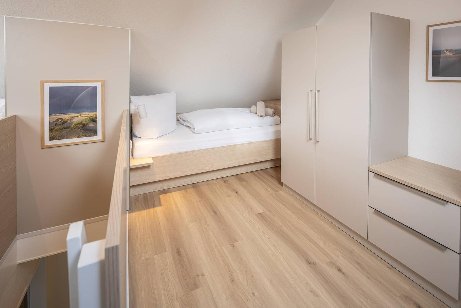 Schlafzimmer mit Bett, Kleiderschrank und Holzboden.