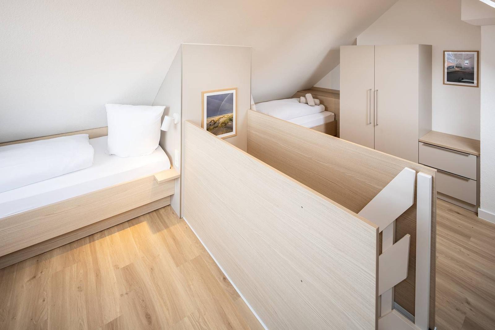 Zimmer mit zwei Betten, Schrank und Tisch. Holzboden und Dachschräge.