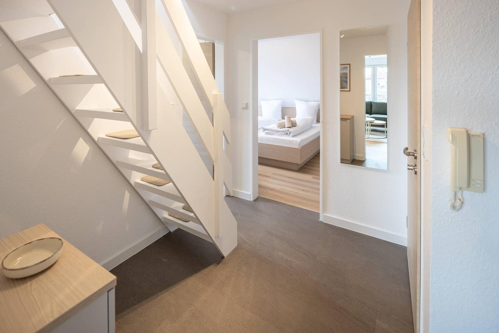 Haus mit Treppe, Schlafzimmer und Spiegel. Holzfußboden und Wandtelefon sichtbar.