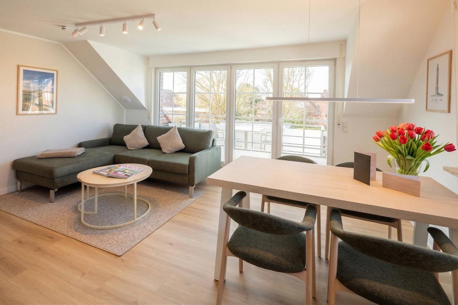 Wohn- und Essbereich mit Sofa, Tisch und Stühlen. Große Fensterfront mit Blick auf Balkon.