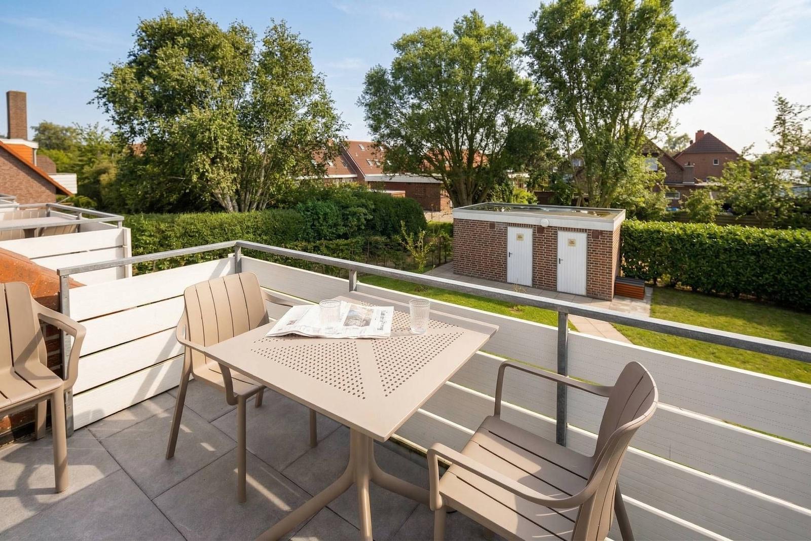 Terrasse mit Tisch und Stühlen, Blick auf Grünflächen und Gebäude.