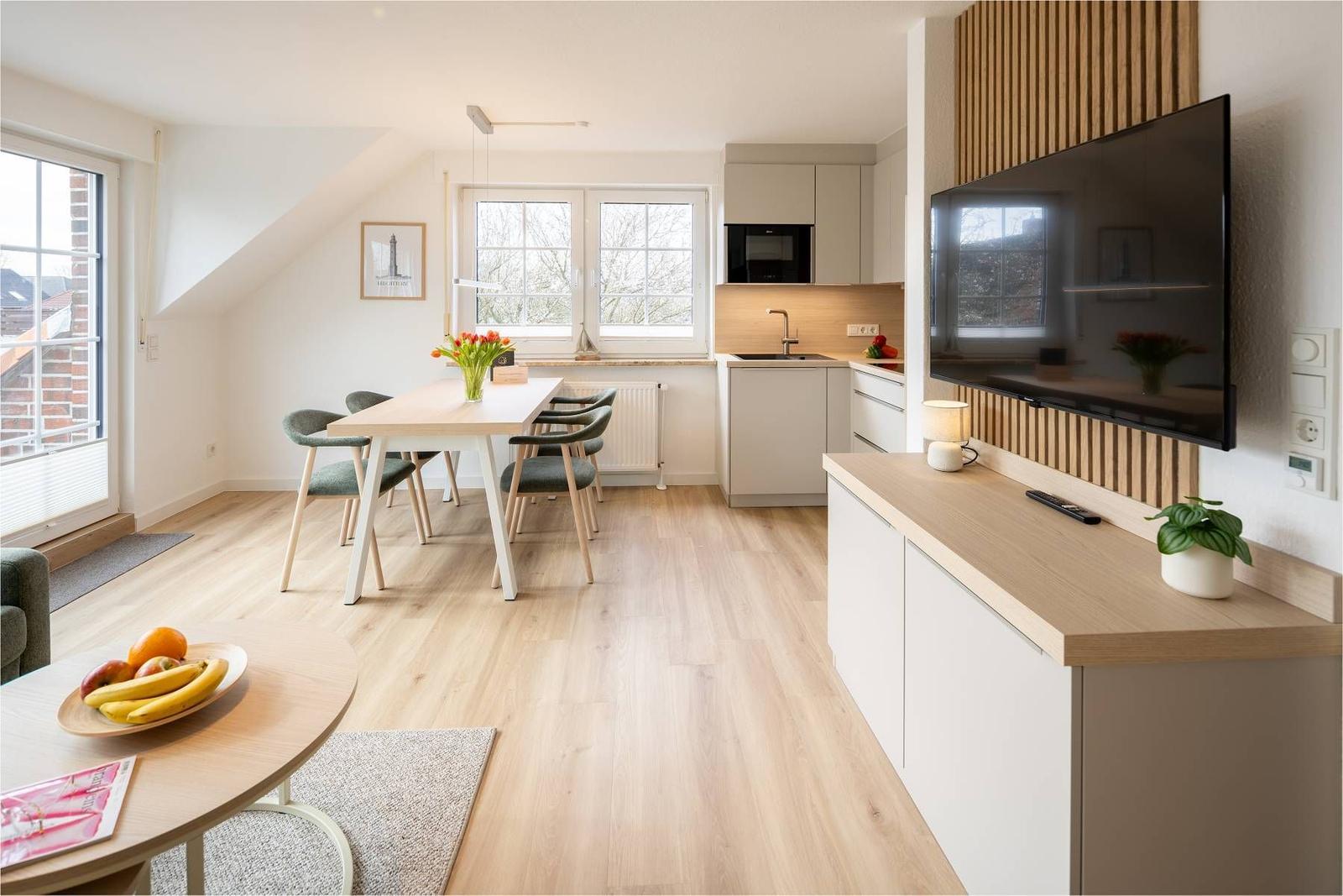 Wohnküche mit Esstisch, TV und Fenstern. Holzboden und moderne Einrichtung.