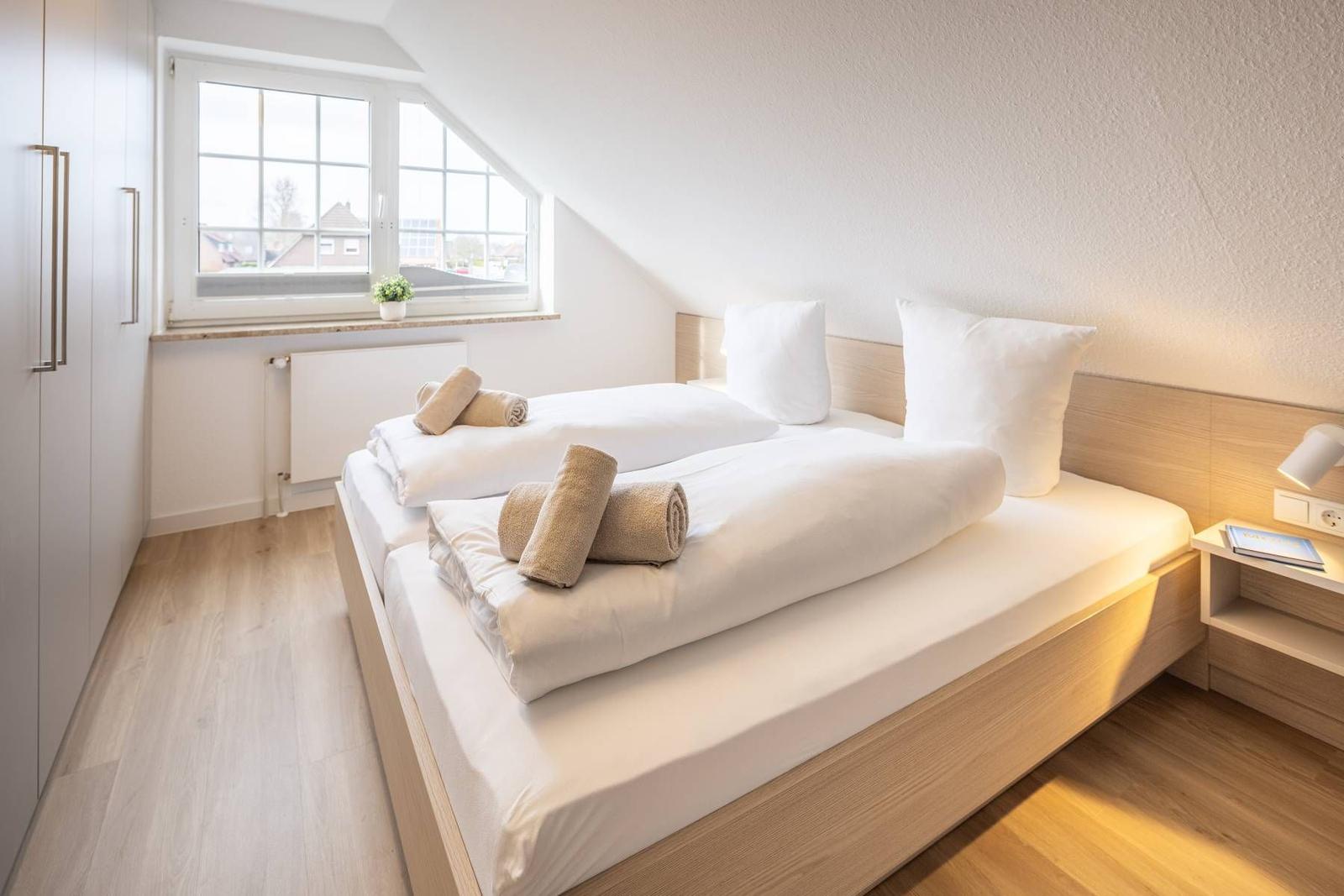 Schlafzimmer mit Doppelbett, Fenster und Nachttisch.