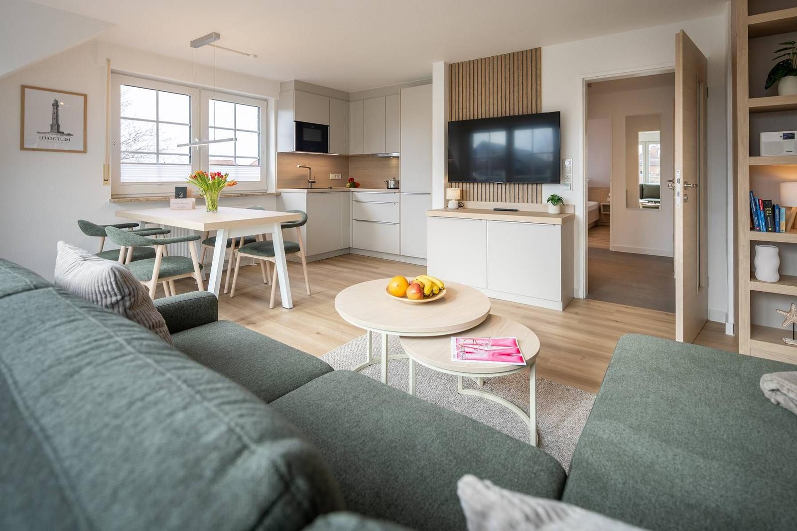 Wohnung mit Küche, Essbereich und Wohnzimmer. Fernseher, Sofa und Tisch sind sichtbar.