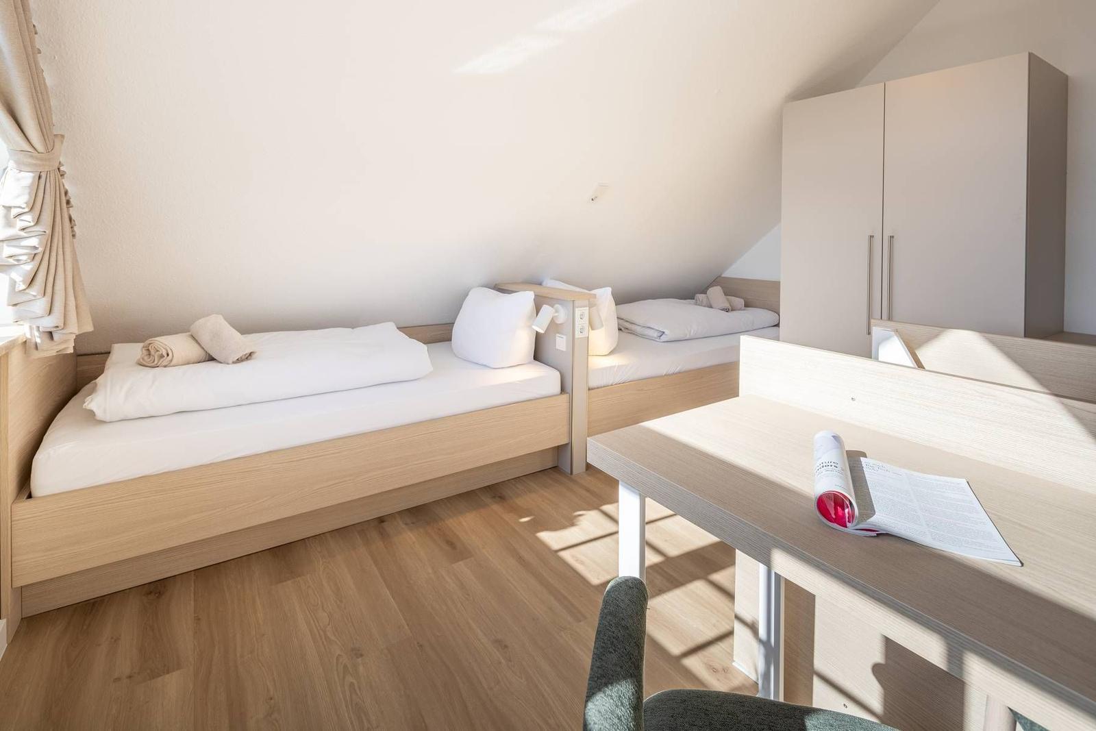 Zimmer mit zwei Betten, Schreibtisch und Kleiderschrank. Holzfußboden und Dachschrägen.