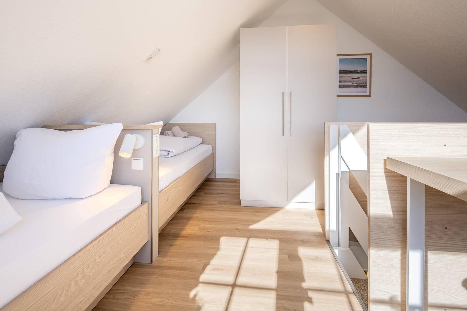 Zimmer mit zwei Betten, Schrank und Tisch unter schrägen Dachdecken.