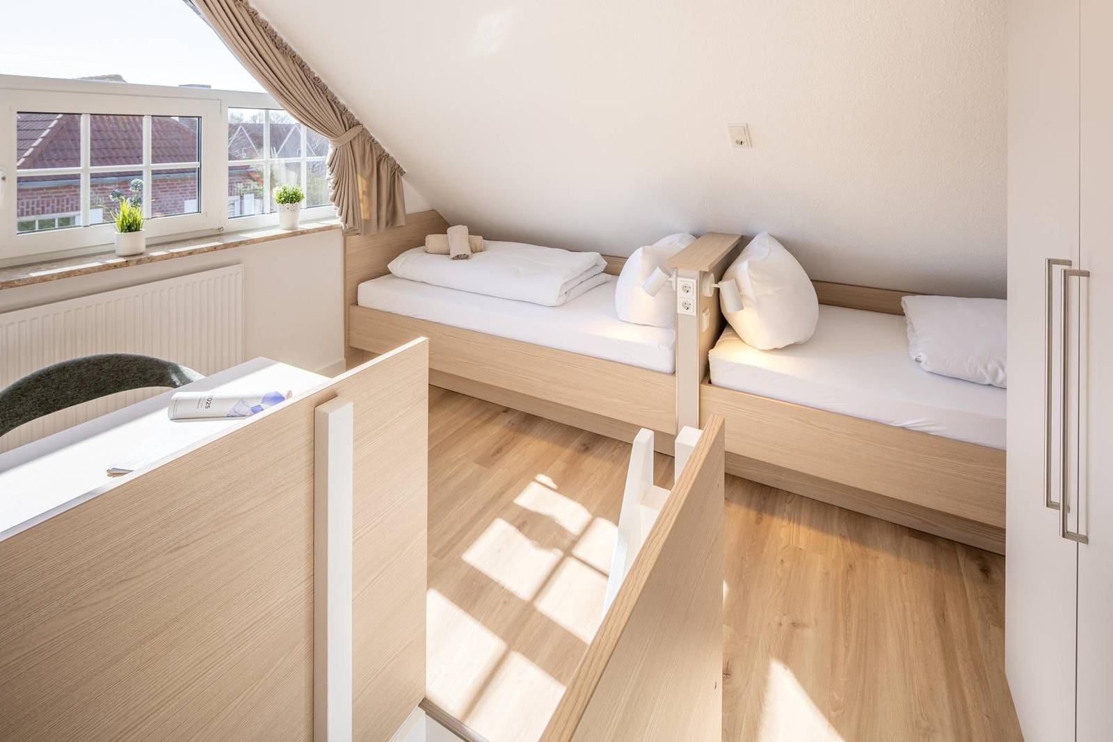 Zwei Einzelbetten unter Dachschräge mit Fenster und Holzboden.