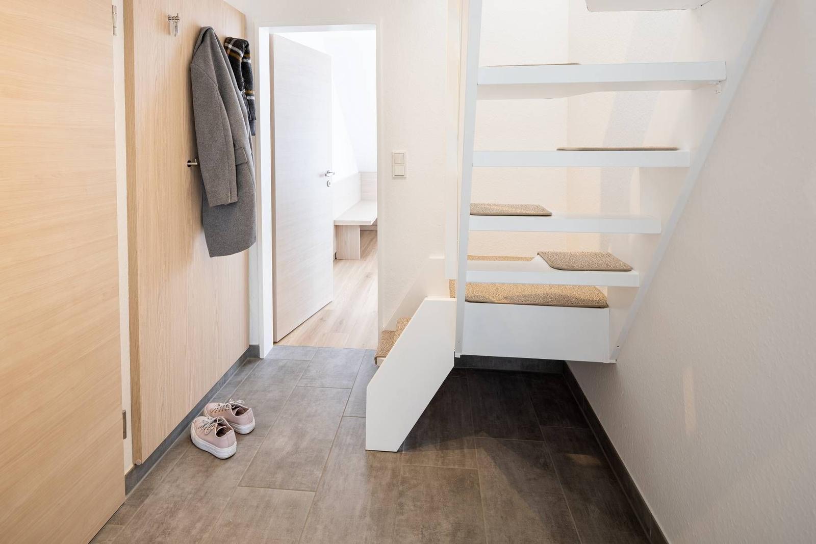 Hausflur mit Treppe und Schuhen an der Wand. Tür führt in das Schlafzimmer.