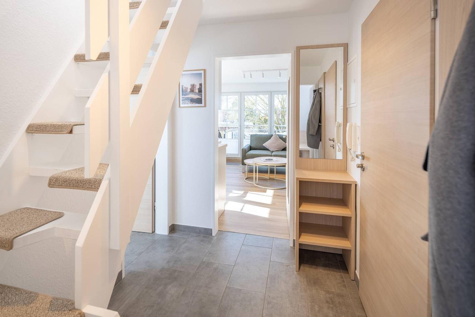 Eingangsbereich mit Treppe, Spiegel und Kleiderständer. Durchgang zur Wohnfläche mit Sofa.