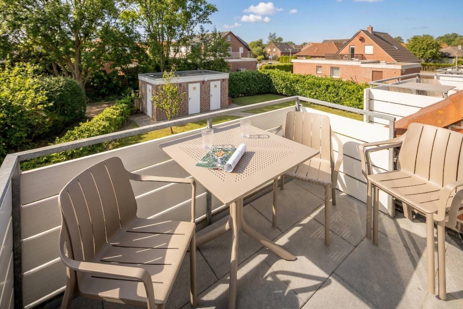 Terrasse mit Tisch und vier Stühlen. Blick auf Grünflächen und Nachbarhäuser.