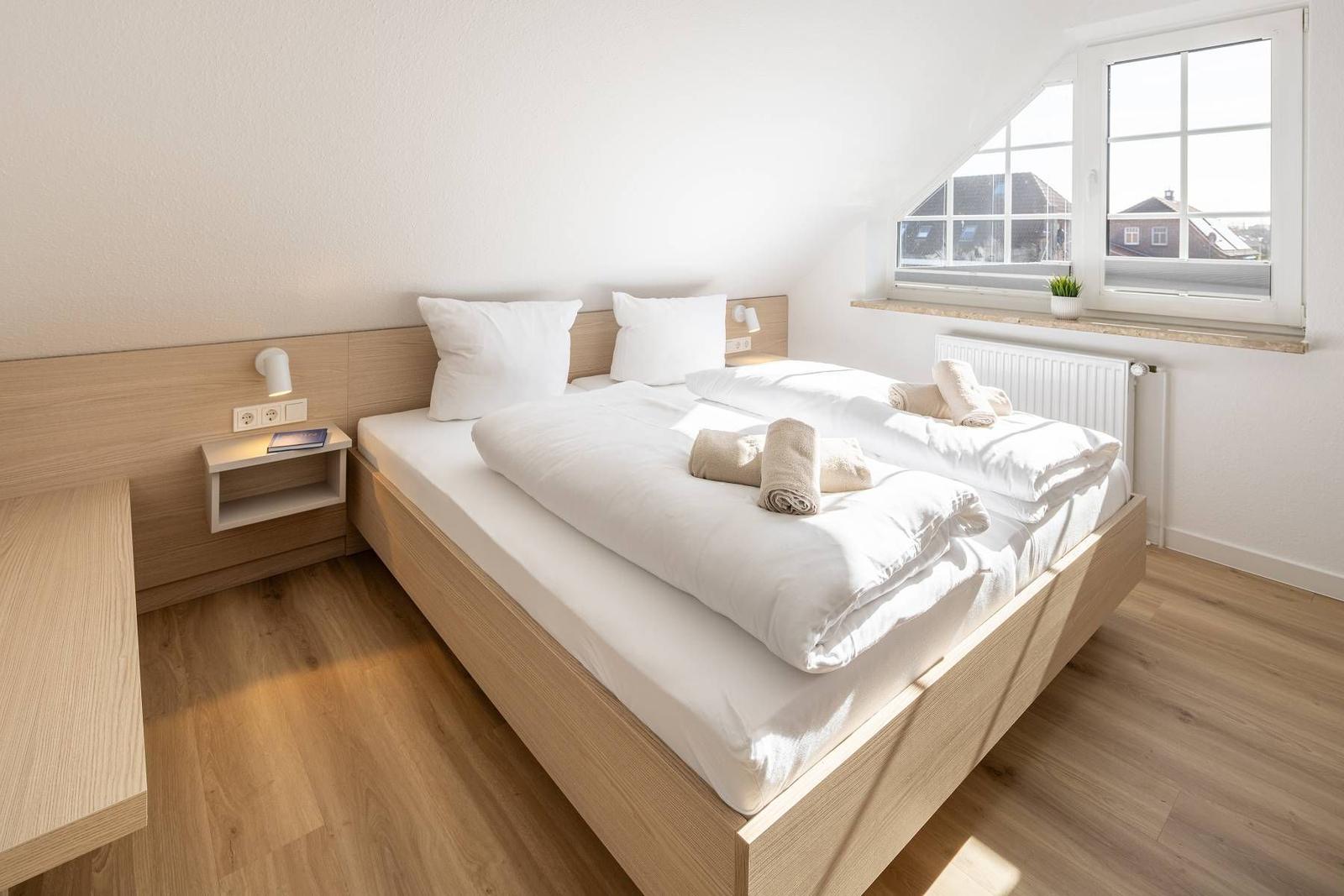 Schlafzimmer mit Doppelbett, Holzboden und Fenster mit Blick auf Dächer.