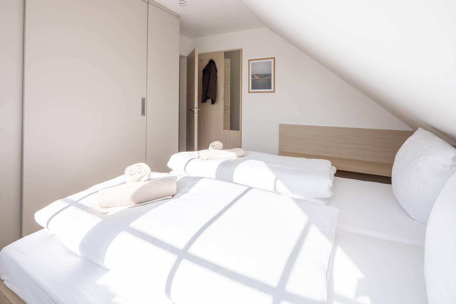 Schlafzimmer mit Dachschrägen, Bett mit weißen Laken und Handtüchern.