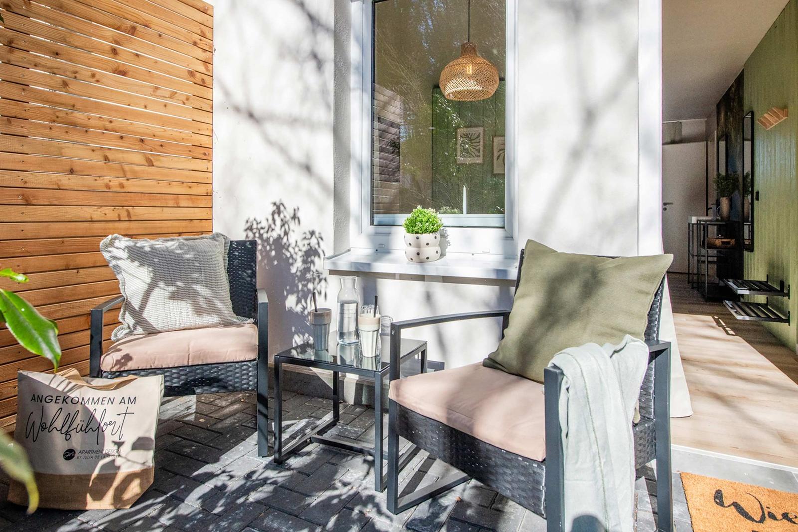 Terrace with two seating areas, table and plant by window. Wooden wall and bathroom visible.
