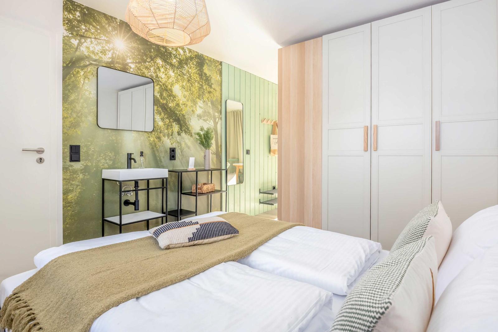 Bedroom with bed, wardrobe, and tree-patterned wall. Shower and sink in adjacent area.